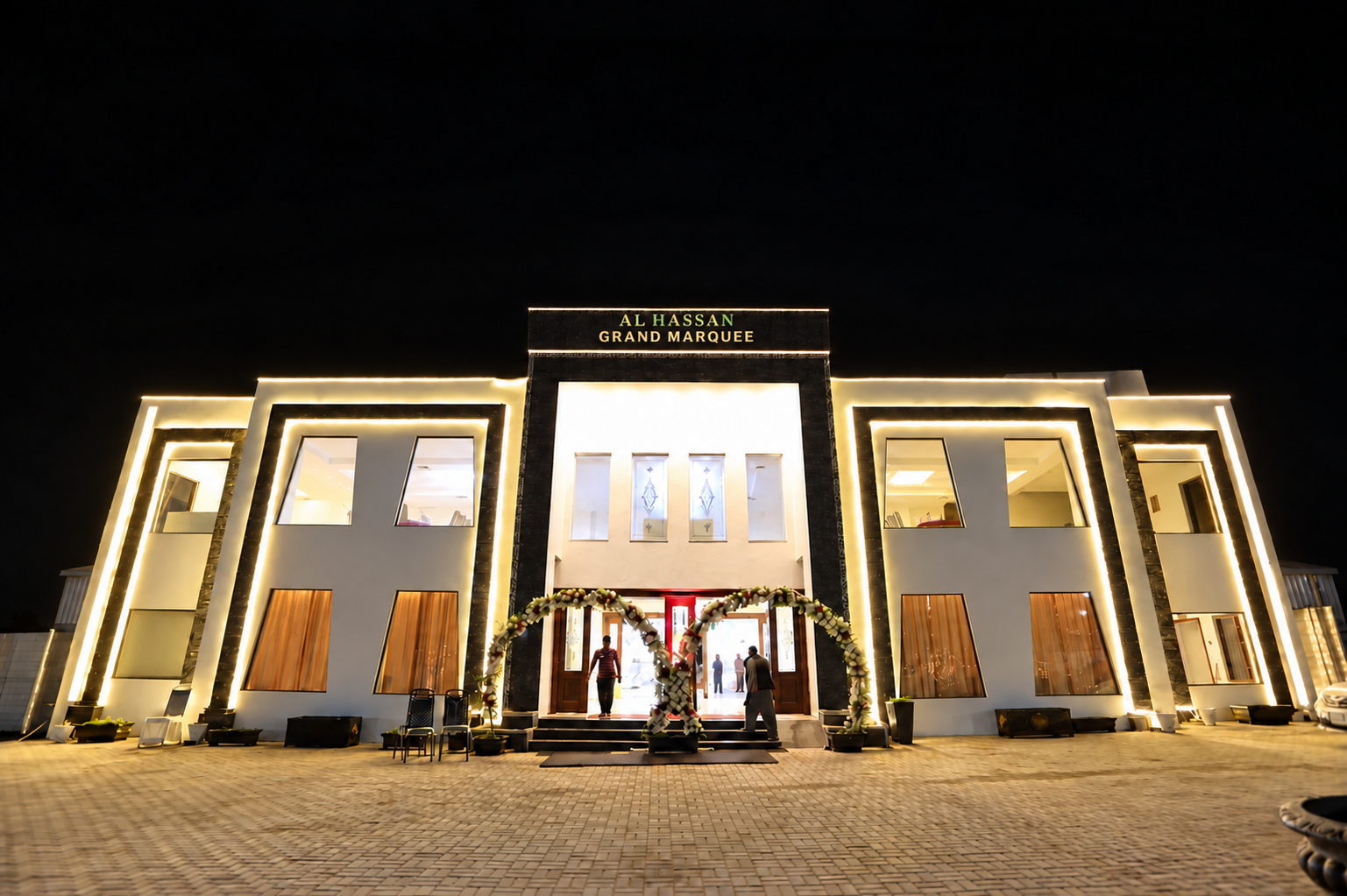 Illuminated night facade of Al Hassan Grand Marquee with floral entrance arch